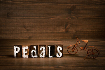 PEDALS. Text from alphabet blocks and rusty miniature bicycle on wood texture background