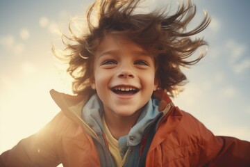 A young boy smiling with his hair blowing in the wind. Perfect for lifestyle and happiness concepts - obrazy, fototapety, plakaty