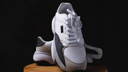A pair of white sneakers with black inserts on a wooden base. Black background. The sneakers have a...