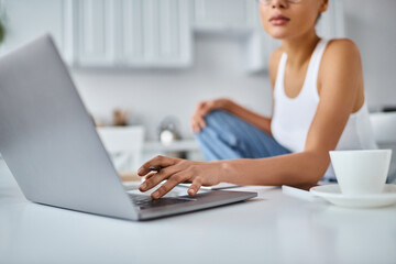 cropped african american freelancer working from home remotely on her laptop, cup of coffee