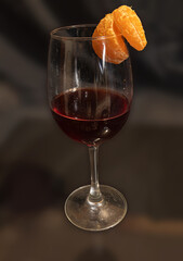 A glass of red wine with a piece of tangerine.