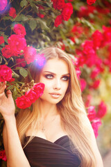Fototapeta premium Beautiful fashionable woman with red lips makeup posing outdoor, in blooming rose garden.