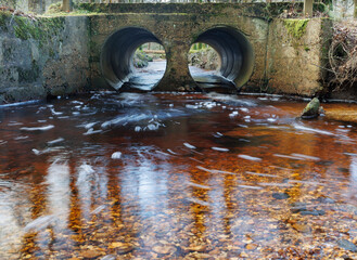 An unusual bridge with two parallel tubes over a small river in the New Forest. Water running...