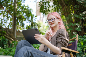 Cute pink hair girl drawing on digital tablet in garden, Woman Doing Freelance Work in Garden,...