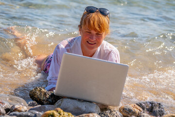 Happy business woman working anywhere and anytime. She working online with laptop on the beach of sea or ocean