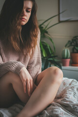 teen girl sitting on bed alone, slumped sad wearing pink knit