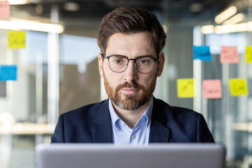 A professional businessman engrossed in work on his laptop at a desk in a bright contemporary...