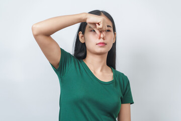 Young Asian frustrated woman with green t-shirt pinches her nose with disgust on her face, reacting...