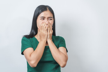 Young Asian frustrated woman with green t-shirt pinches her nose with disgust on her face, reacting to a bad smell in isolation over background.