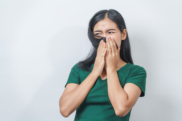 Young Asian frustrated woman with green t-shirt pinches her nose with disgust on her face, reacting...