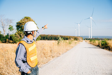 Technician in hardhat inspects windmill farm for clean energy. An Asian engineer ensures turbine...