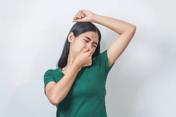 Poster Young Asian frustrated woman with green t-shirt pinches her nose with disgust on her face, reacting to a bad smell in isolation over background. © NanSan