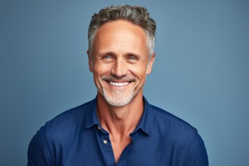 Portrait of a handsome mature man smiling at the camera against blue background - obrazy, fototapety, plakaty