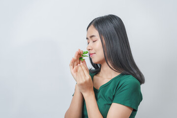 Naklejka premium Beautiful young Asian woman in green t-shirt inhaling the aroma of herbal mint isolated on white background.