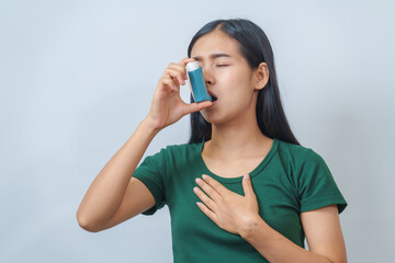Young Asian woman wearing green t-shirt using asthma inhaler isolated on white background, indoors,...