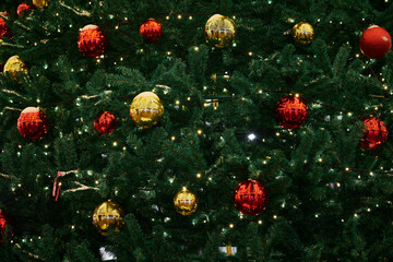 Festive New Year Christmas tree decorated red yellow Christmas balls with garlands lights, close up...