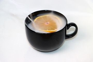 hot tea with oranges from which it is smoking in a black mug on a white background