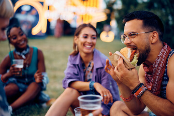 Young festival goer eating hamburger with friends.