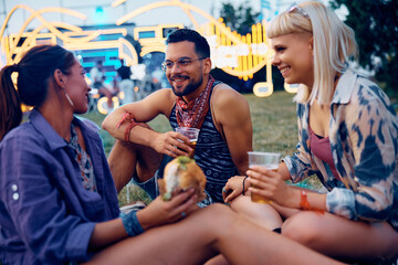 Happy festival goer and his female friends drinking beer and eating burgers outdoors.