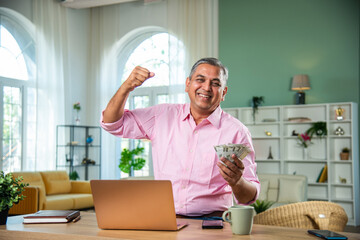Indian mid age man holding currency notes or money while working on laptop in living room