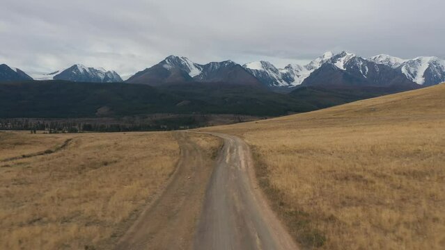 Vintage gray van car riding on meadow dirt road with dust surrounded by cinematic alpine valley drone shot. Automobile transportation movement on sand path at beautiful cliff rock scenery travel trip