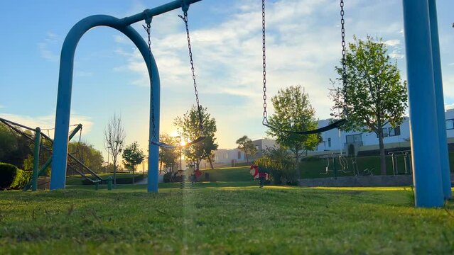 Columpio en movimiento solo al amanecer con sol de fondo en parque infantil con instalaci&oacute;n de juegos divertida de ni&ntilde;os 