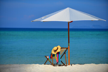 Beach chair with accessories under the big white parasol in front of the beatiful sea.