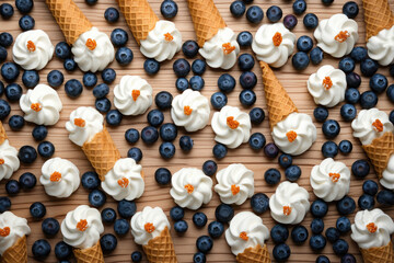 Overhead view of whipped cream dollops and blueberries on waffle cones, artistically arranged on a...