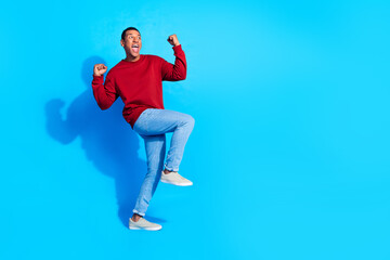 Full length photo of satisfied crazy person raise fists achievement look empty space isolated on blue color background