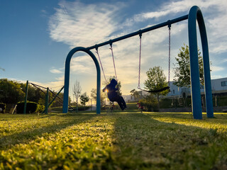 Niño feliz divertido en el columpio disfrutando temprano el amanecer al aire libre en el parque de...