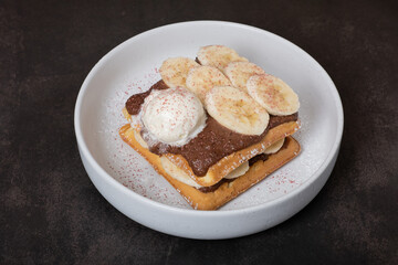 Belgian waffles with banana and chocolate sauce on a dark background