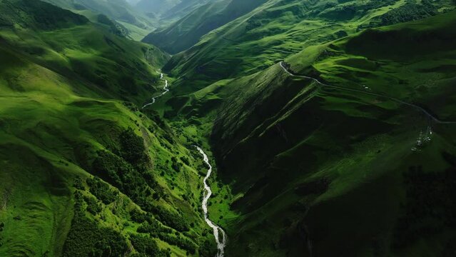 Winding river cutting through lush green mountain valleys with a narrow road paralleling the flow