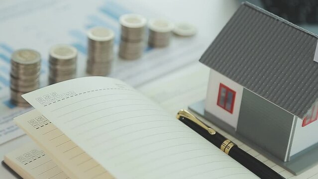 Real estate concept background. House model and coins stack on wooden table, copy space.