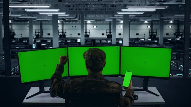 Back View Of Happy Asian Military Looking At Mobile Phone Green Screen And Celebrating While Working With Multiple Computer Monitor In Data Center