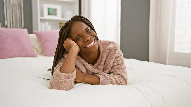 Smiling woman with braids lying comfortably in a cozy bedroom, reflecting relaxation and modern home interior design.