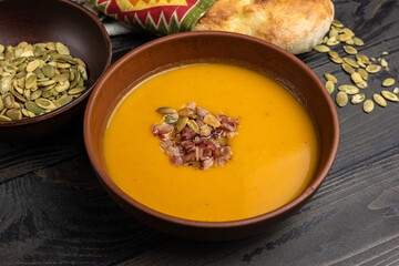 Pumpkin soup with bacon and pumpkin seeds on wooden background.