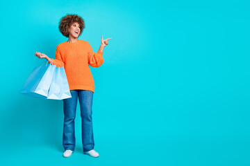 Full size portrait of cheerful lovely girl hold mall bags look direct finger empty space isolated on turquoise color background