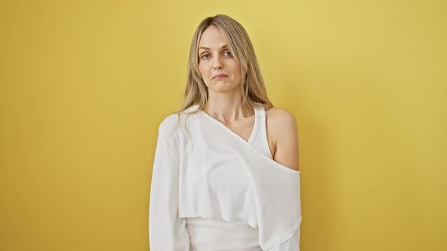 Furious blonde bombshell letting it all out! young woman screaming, shout echoing over yellow background. rage personified, loud communication, hand on mouth.