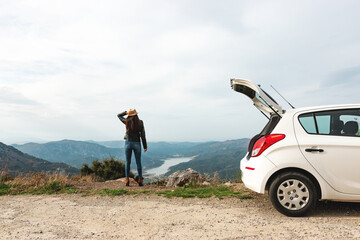 Woman traveler near to the hatchback car with mountain background.