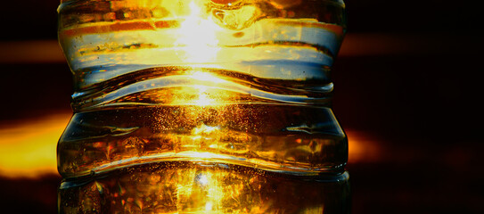 Parte de botella de agua de plástico con el sol del atardecer captado por detrás, Abstracta  - obrazy, fototapety, plakaty