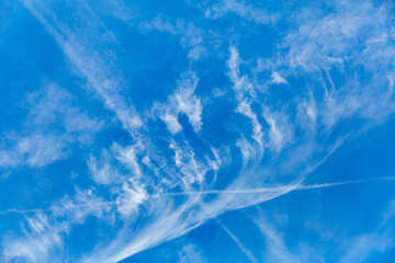 Cirrus clouds and water vapor trails left by airplanes against clear blue sky in background in...
