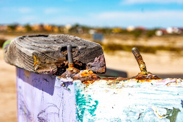 Closeup of two rusty screws and a piece of wood on edge of boat hull against blurred background,...