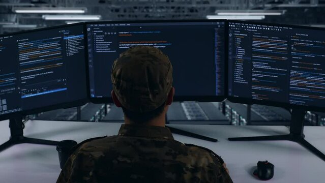 Back View Of Tired Asian Military Stretching While Write Code With Multiple Computer Screens In Data Center