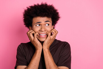 Close up photo of young upset guy afraid bite nails looking empty space panic too much problems isolated over pink color background