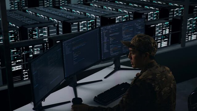 Side View Of Asian Military Drinking Coffee And Using Computer To Write Code With Multiple Screens In Data Center