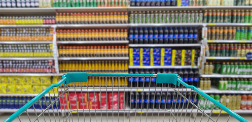 Green shopping cart with blurred image of beverage on shelf in background. (Selective focused at shopping cart)