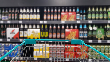 Green shopping cart with blurred image of alcohol store in background. (Selective focused at shopping cart).