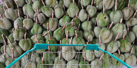 Green shopping cart with pile of durian fruit in background.