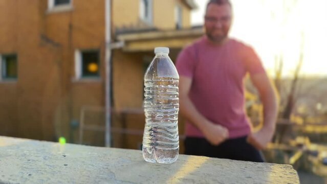 A man shows off his skills by completing a water bottle flip trick outside at dusk.	