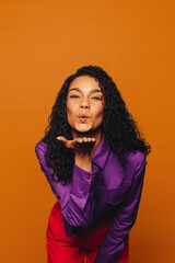 Young woman with curly hair blowing a kiss in bright colorful studio - fashionable hipster style